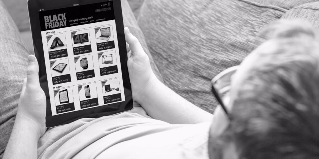 Man browsing Black Friday deals on a tablet while sitting on a couch.